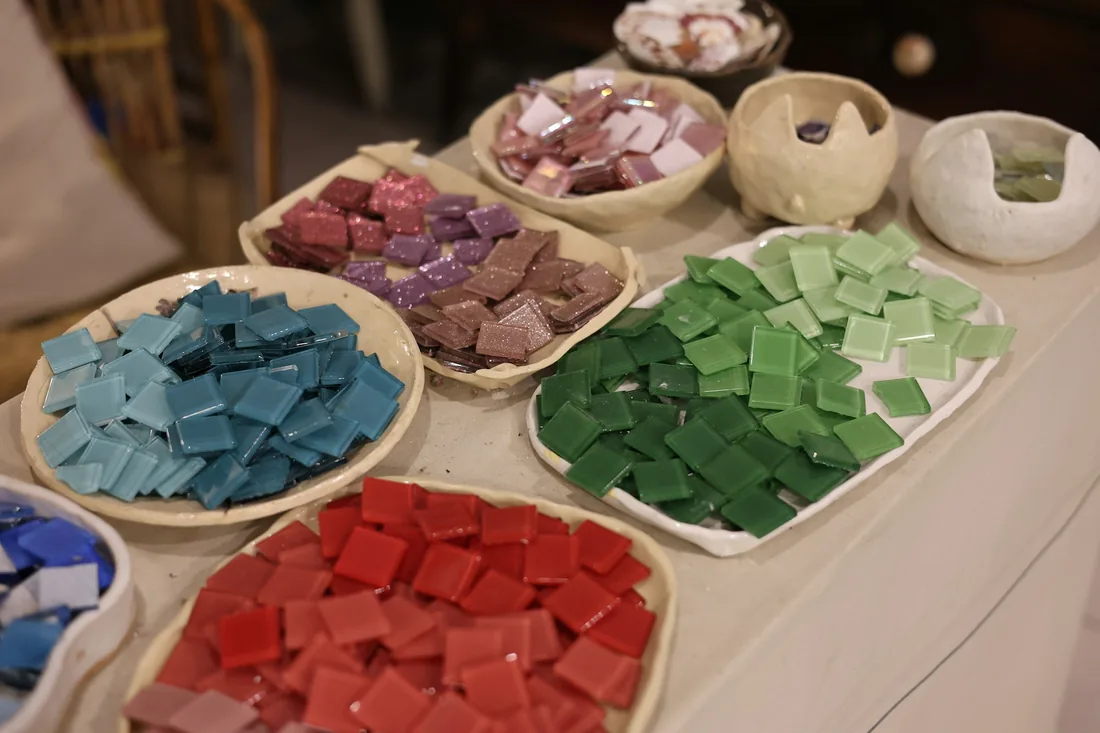 Cuencos de cerámica con teselas de pasta vítrea separadas por colores sobre una mesa de taller
